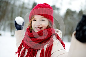 Adorable little girl having fun in beautiful winter park. Cute child playing in a snow.