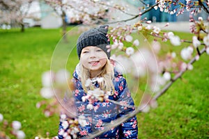 Adorable little girl having fun in blooming cherry garden on beautiful spring day