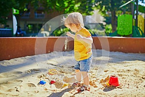 Adorable little girl having fun on playground in sandpit