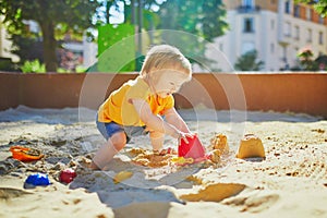 Adorable little girl having fun on playground in sandpit