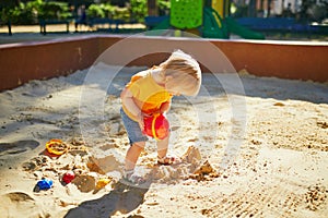 Adorable little girl having fun on playground in sandpit