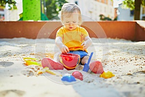 Adorable little girl having fun on playground in sandpit