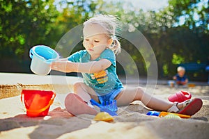 Adorable little girl having fun on playground in sandpit