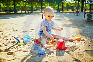 Adorable little girl having fun on playground in sandpit