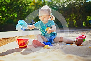 Adorable little girl having fun on playground in sandpit