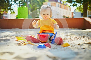 Adorable little girl having fun on playground in sandpit