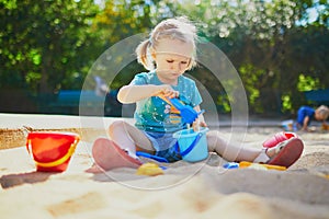 Adorable little girl having fun on playground in sandpit