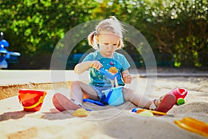 Adorable little girl having fun on playground in sandpit