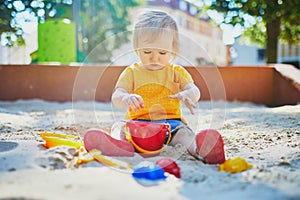 Adorable little girl having fun on playground in sandpit