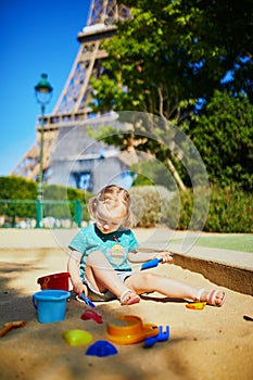 Adorable little girl having fun on playground in sandpit near the Eiffel tower