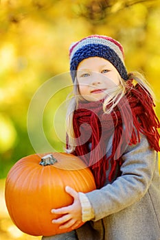 Adorable little girl having fun on a pumpkin patch on beautiful autumn day