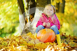 Adorable little girl having fun on a pumpkin patch on beautiful autumn day