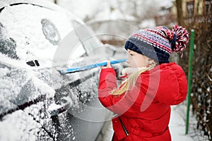 Adorable little girl helping to brush a snow from a car. Mommy`s little helper.