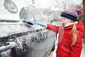 Adorable little girl helping to brush a snow from a car. Mommy`s little helper.