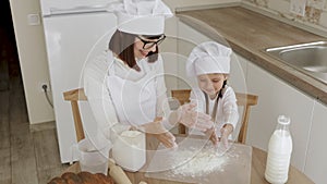 Adorable Little Girl And Her Caucasian Mom in hats of chef clapping their hands with flour