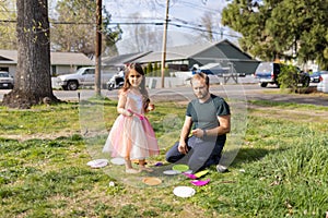 Adorable little girl and her father cutting colorful paper plates in front yard