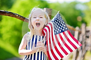 Adorable little girl holding american flag outdoors on beautiful summer day