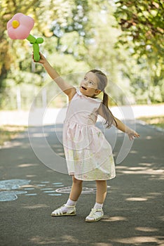 Adorable little girl holding flower shape balloon outdoors in summer park