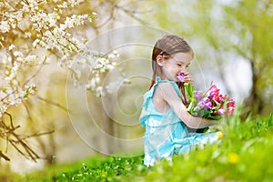 Adorable little girl holding tulips for her mother in blooming cherry garden