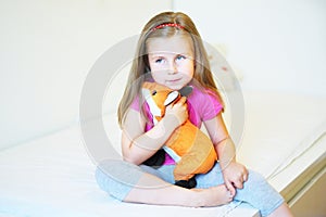 Adorable little girl hugging fox plush toy in bed