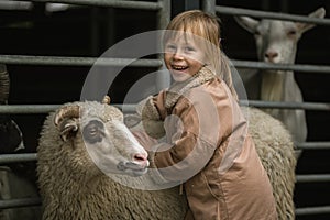 Adorable little girl hugs cute white sheep in the farmland. Happy little caucasian girl petting a sheep at the farm