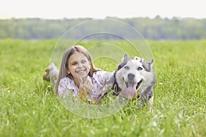 Adorable little girl with Husky dog lying on green meadow outside. Lovely child with her pet in countryside