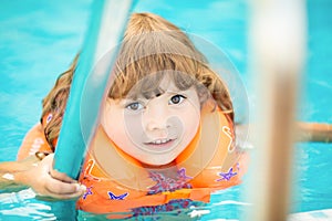 Adorable little girl with inflatable life vest having fun in the pool