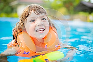 Adorable little girl with inflatable life vest having fun in the pool