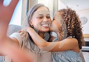 Adorable little girl kissing her mother on the cheek while they take a selfie together. Young mom holding cellphone and