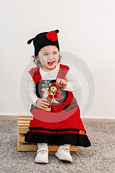 Adorable little girl with ladybug costume sitting on wooden box and holding her doll.