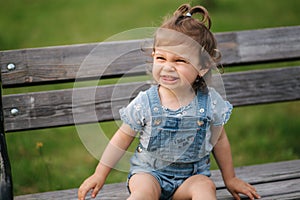 Adorable little girl laughing. Beautiful female kid in denim sitting on the bench in park. Happy little girl smile