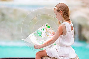 Adorable little girl looking at touristic map near Trevi Fountain, Rome, Italy. Happy toodler kid enjoy italian vacation