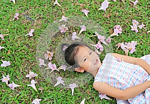 Adorable little girl lying on green grass with fall pink flower in the garden outdoor