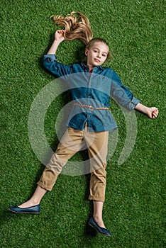 Adorable little girl lying on green grass and looking at camera