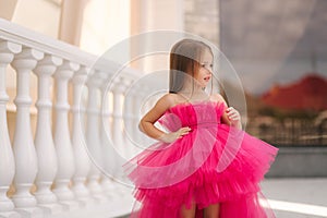 Adorable little girl model in pink fluffy dress walkin outdoors by the restaurant. Happy little kid. Space for text