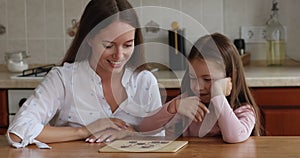 Adorable little girl and mother playing checkers at home