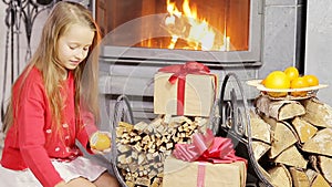 Adorable little girl opening christmas gifts near fireplace