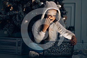 Adorable little girl opening a magical Christmas gift by a Christmas tree