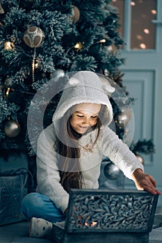 Adorable little girl opening a magical Christmas gift by a Christmas tree