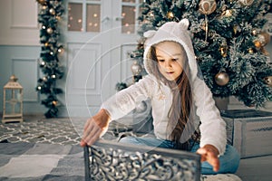Adorable little girl opening a magical Christmas gift by a Christmas tree