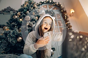 Adorable little girl opening a magical Christmas gift by a Christmas tree