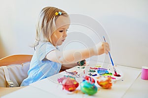 Adorable little girl painting eggs for Easter