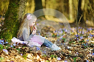 Adorable little girl picking the first flowers of spring in the woods on beautiful sunny spring day