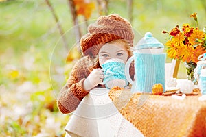 Adorable little girl on picnic in autumn park. Cute little girl  having tea party outside in the autumn garden.  Girl drinking tea