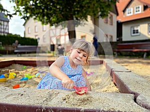 Adorable little girl on playground in sandpit. Toddler playing with sand molds and making mudpies. Outdoor creative