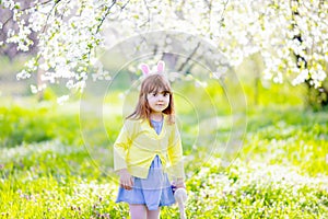 Adorable little girl playing in blooming apple tree garden on Easter egg hunt. Child in spring fruit orchard with cherry blossom