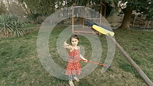 Adorable little girl playing with a broom in big backyard