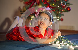 Adorable little girl playing with Christmas lights near the tree