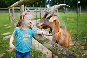 Adorable little girl playing with goats and sheep at farm