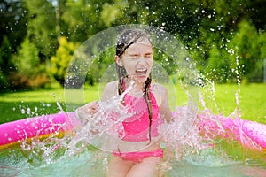 Adorable little girl playing in inflatable baby pool. Happy kid splashing in colorful garden play center on hot summer day.